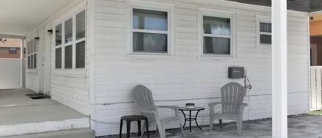 Ein eingeschossiges Haus mit Veranda, zwei Fenstern und einem kleinen Tisch mit Stühlen.