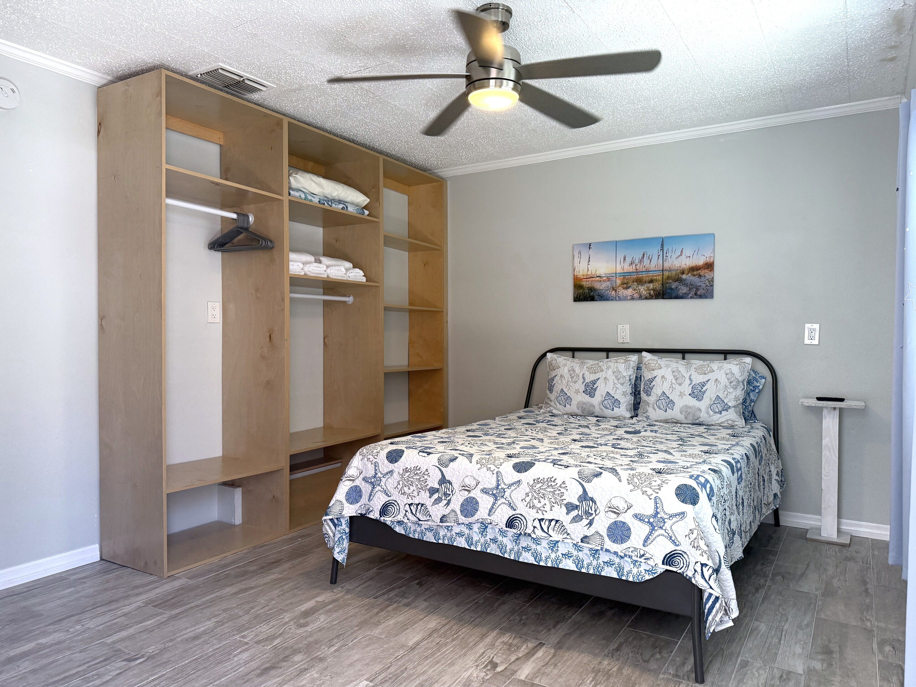 Een slaapkamer met een bed, een houten kledingkast, een plafondventilator en een schilderij aan de muur.