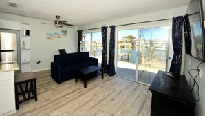 Un salón moderno con un sofá azul oscuro, una mesita y una cocina con refrigerador.