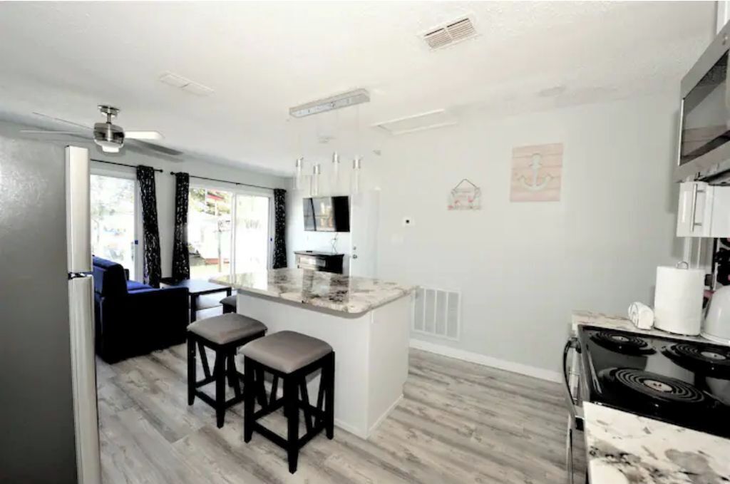 A modern kitchen with a central island, bar stools, a stove, and a dining area with a sofa and table.