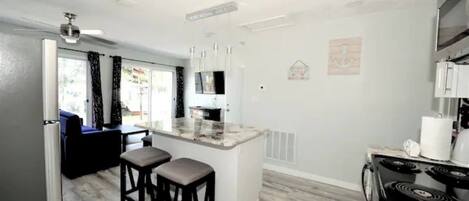 A modern kitchen with a central island, bar stools, a stove, and a dining area with a sofa and table.