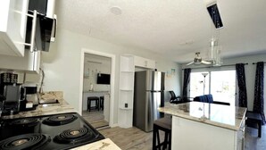 Una cocina moderna con estufa, refrigerador y una isla. Hay un ventilador de techo y una ventana con cortinas.