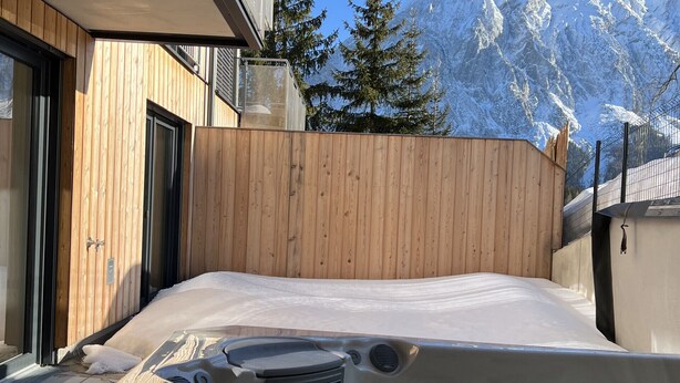 Un jacuzzi con muelle de madera y vistas a montañas nevadas.