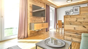 Una sala de estar moderna con paredes de madera, un televisor grande y un comedor con mesa y sillas.