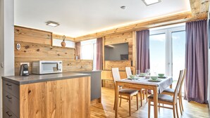 Una cocina moderna con detalles de madera, un comedor con una mesa lista para cuatro personas y un ventanal con cortinas.