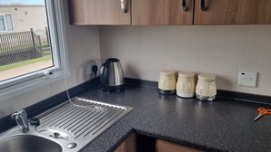 A kitchen with a stainless steel sink, a kettle, and four coffee containers on the counter. - Lovely 8 Berth Direct Beach Access (Skegness)