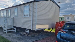 A mobile home with a front porch, a small staircase, and a visible propane tank. - Lovely 8 Berth Direct Beach Access (Skegness)