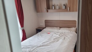 A bedroom with a wooden headboard, a bedside table, and a shelf above the bed. - Lovely 8 Berth Direct Beach Access (Skegness)