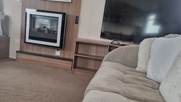A cozy living area with a flat-screen TV mounted on the wall, a comfortable sofa, and a small wooden cabinet. - Lovely 8 Berth Direct Beach Access (Skegness)
