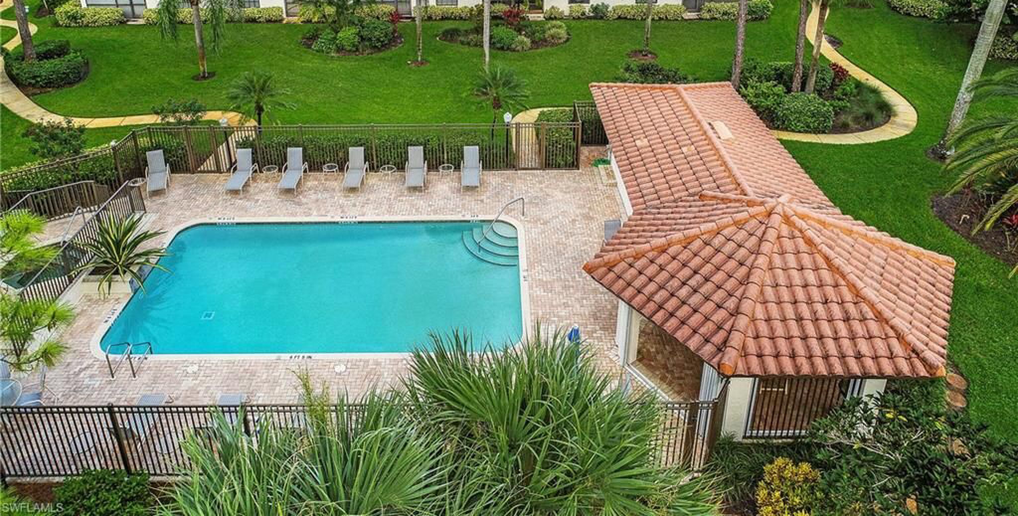 Una piscina con sillas de descanso, rodeada de un césped cuidado y palmeras.