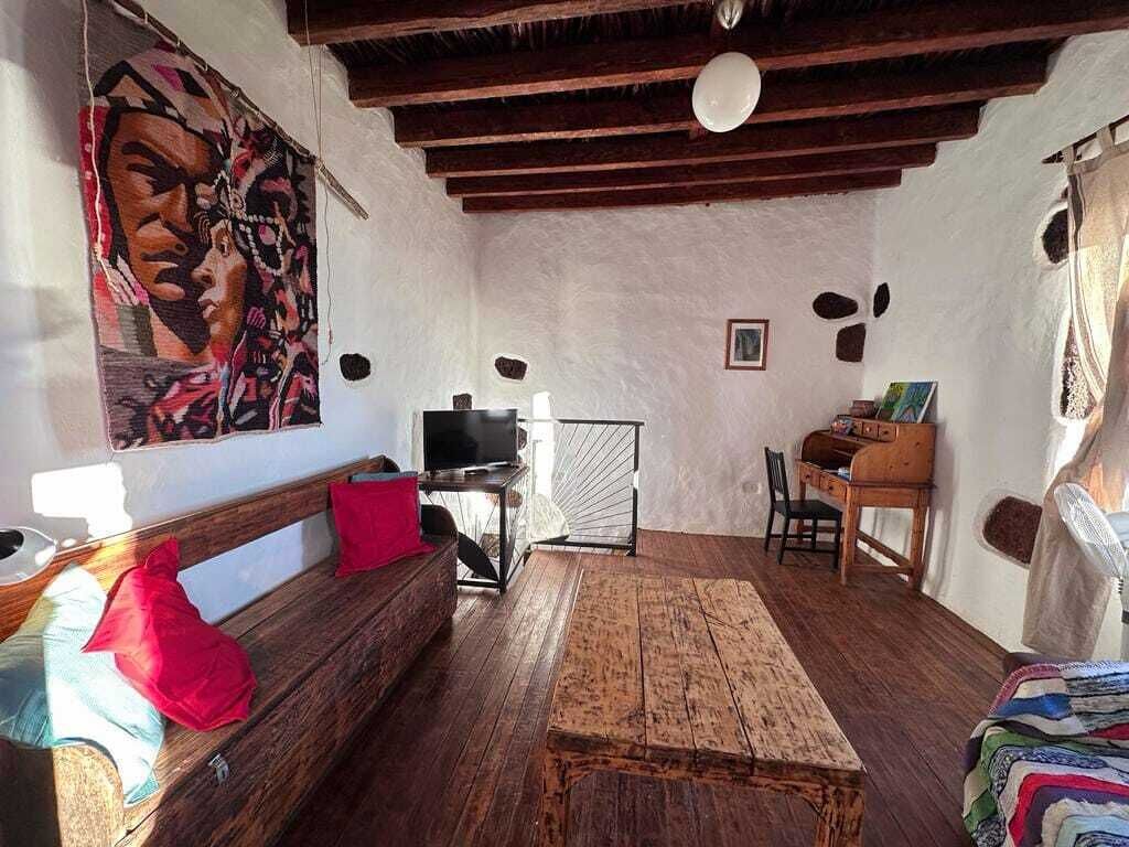 Een knus ingerichte kamer met een houten bankje, een tafeltje, een televisie en een schilderij aan de muur.
