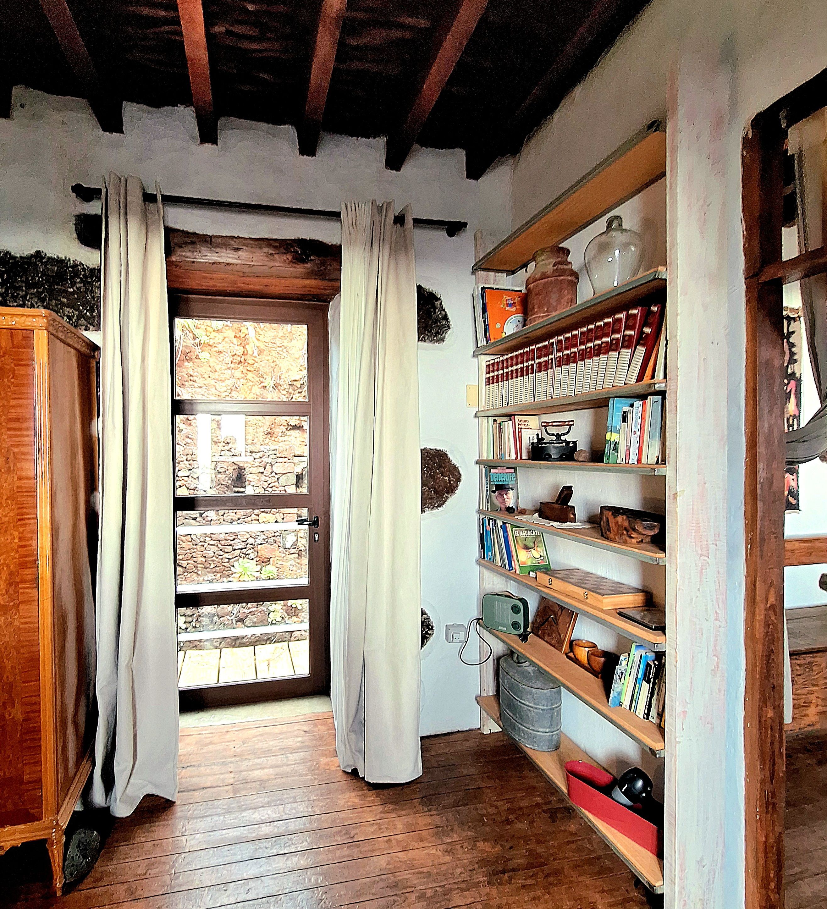 Un couloir étroit au plancher en bois, une porte en bois ornée de rideaux et une bibliothèque remplie de livres et de divers objets.