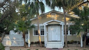 A single-story house with a front porch, a white picket fence, and a small garden with palm trees and shrubs. - Tranquil Beauty-Private Pool - Outside Lanai-Beaches Nearby (Key West)