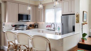 A modern kitchen with white cabinetry, stainless steel appliances, wicker chairs, and pendant lighting. - Tranquil Beauty-Private Pool - Outside Lanai-Beaches Nearby (Key West)