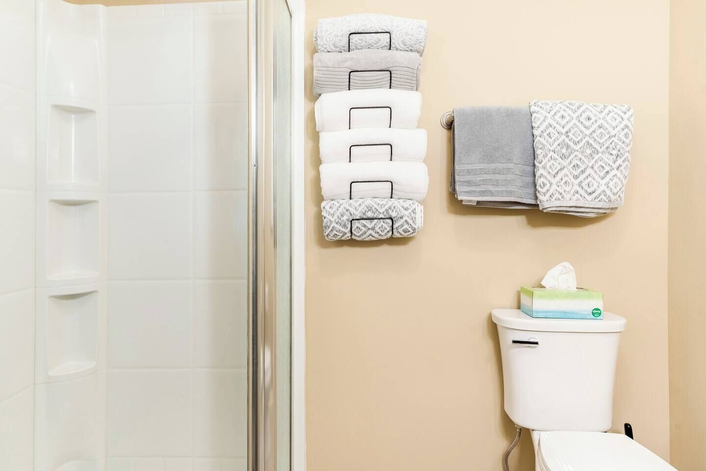 A bathroom with a glass shower door, a toilet with a tissue box, and towels on a rack.