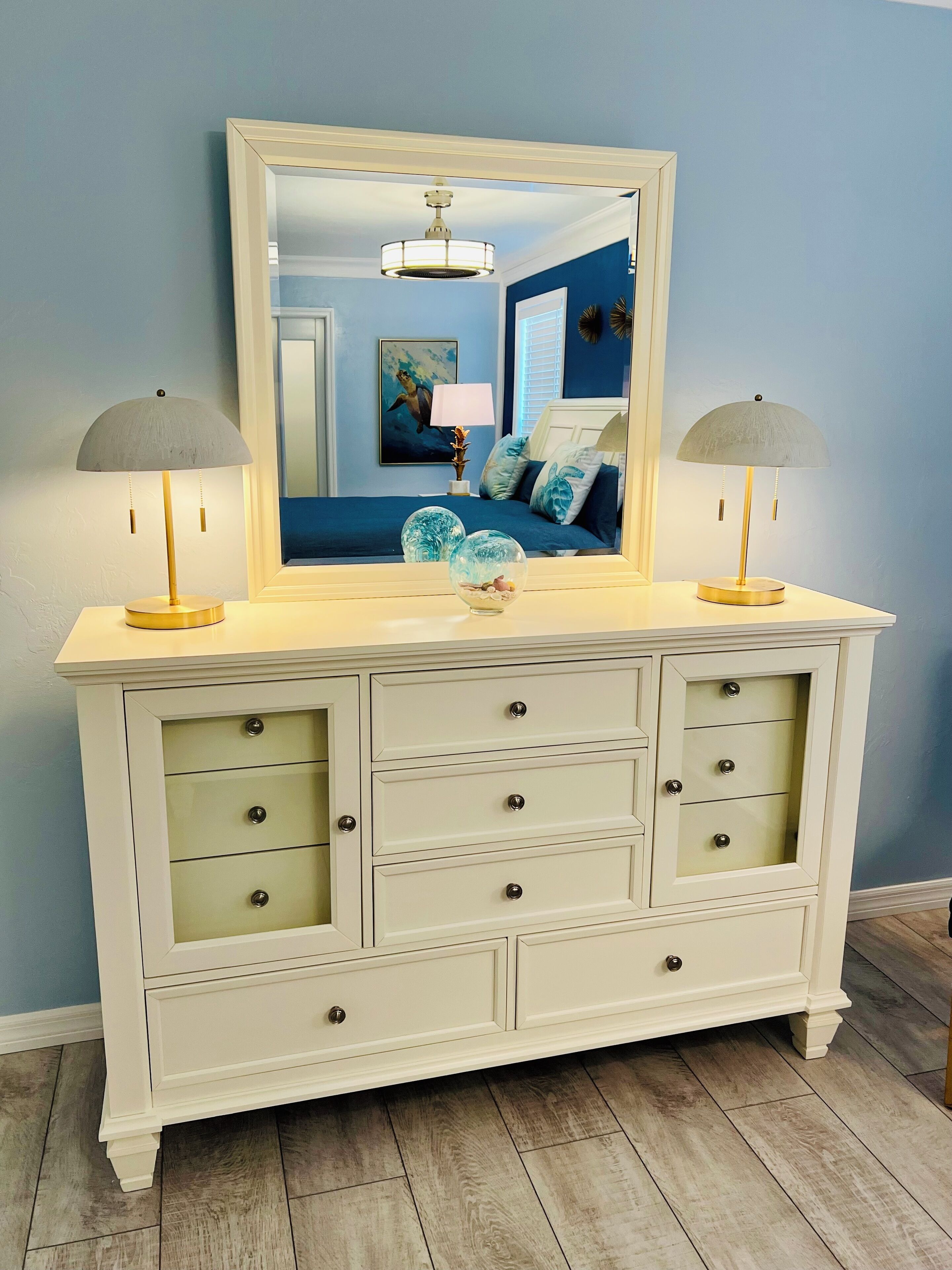 A white vanity with a large mirror, two lamps, and a decorative bowl on the counter.