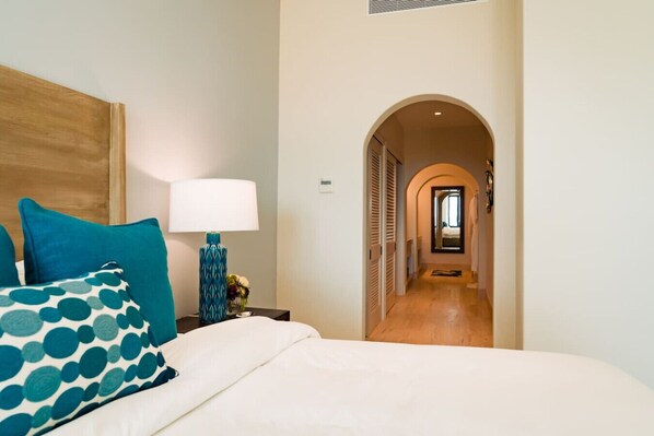 A hotel room with a bed, a nightstand with a lamp, and a hallway leading to another room. - Villa Paloma · Cabo del Sol villa 5BD private Pool, beach access (Cabo San Lucas)