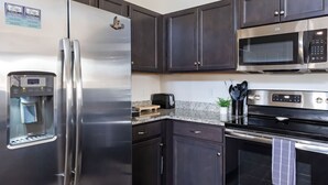 Eine Küche mit einem Edelstahl-Kühlschrank, einer Mikrowelle, einem Backofen, dunklen Schränken und einer Kaffeemaschine.