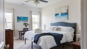 Ein Schlafzimmer mit einem Bett, einem Schreibtisch, einem Stuhl, einem Deckenventilator und Kunstwerken an den Wänden.
