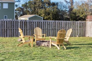 Un jardin avec une terrasse en bois, trois chaises Adirondack et un foyer extérieur.