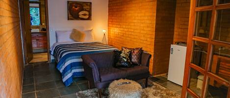 A compact bedroom with a bed, a sofa, a small stool, and a refrigerator.