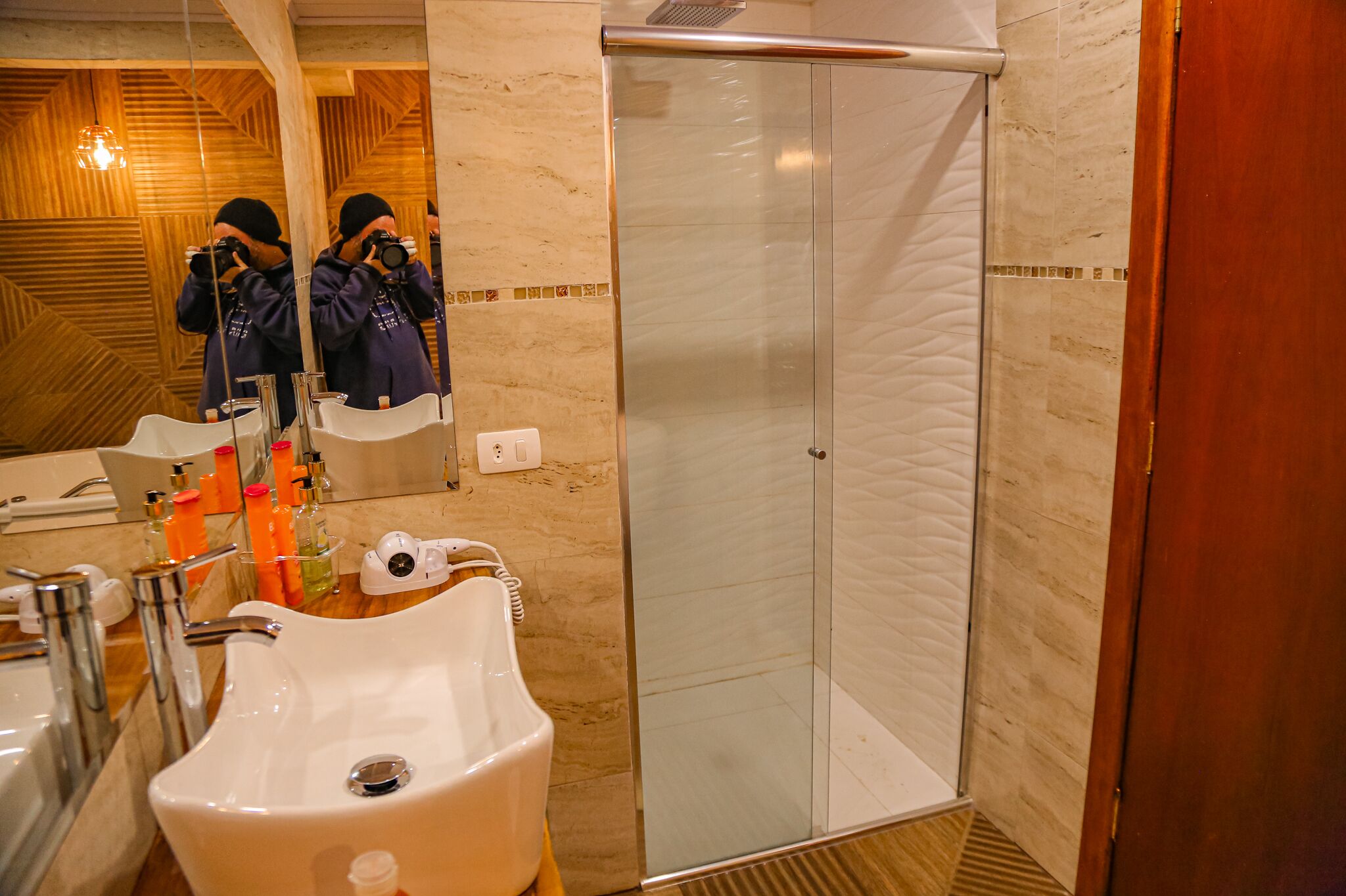 A bathroom with a large mirror, a sink, a glass shower enclosure, and toiletries on the counter.