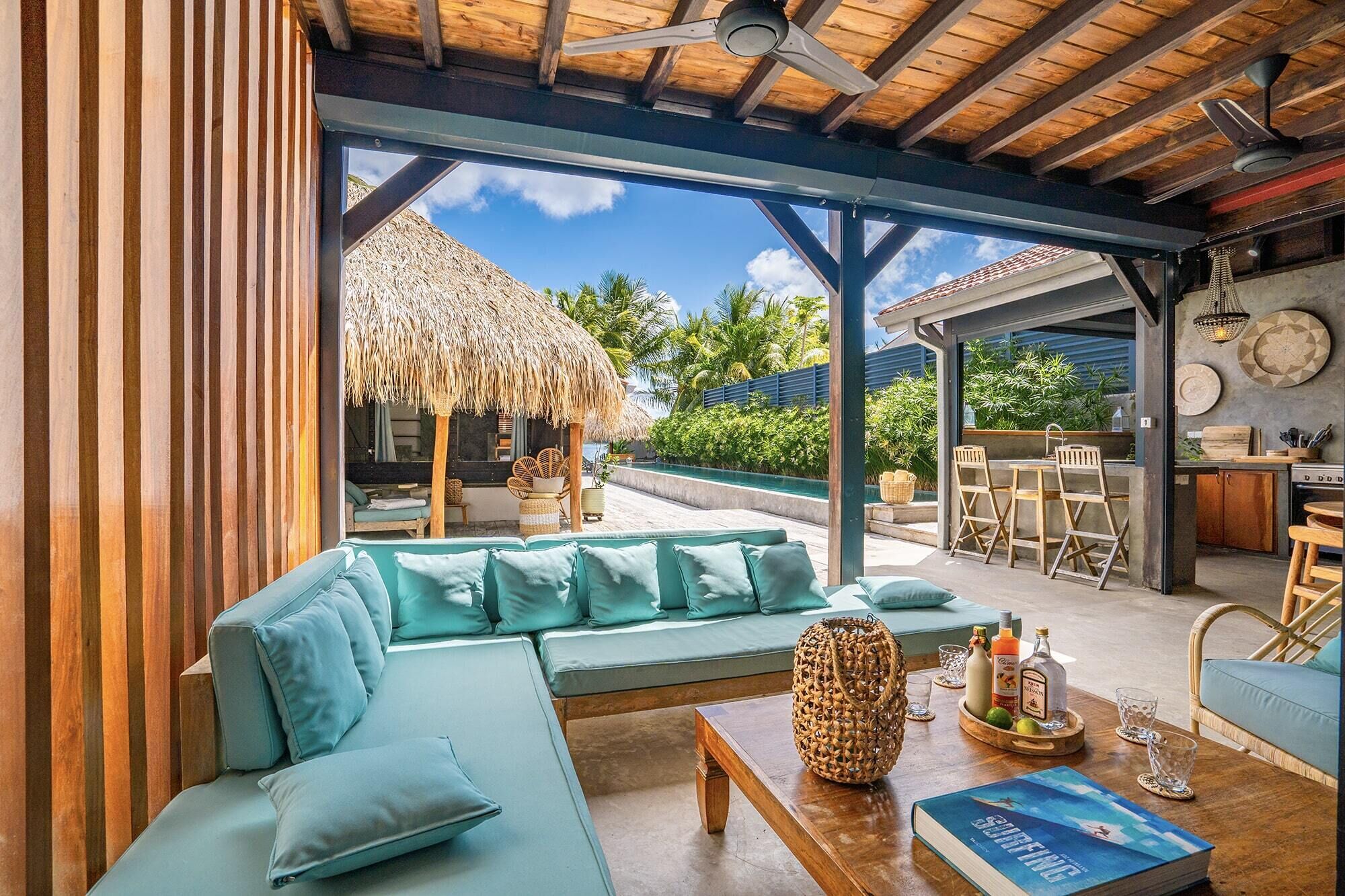 A modern outdoor seating area with a thatched-roof structure, a pool, and a dining setup.