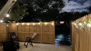 A wooden deck with a concrete pathway, two black chairs, and a small table. - Delightful and cozy RV with outdoor space (St. Petersburg)