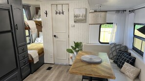 A compact RV interior with a kitchenette, a dining area, and a seating space with a view of the outdoors. - Delightful and cozy RV with outdoor space (St. Petersburg)