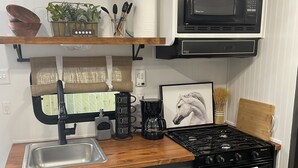 A compact kitchen with a sink, stove, microwave, and a coffee maker. - Delightful and cozy RV with outdoor space (St. Petersburg)