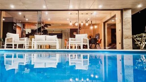 Un área de piscina interior moderna con vista despejada, sillas reclinables blancas y una escalera que lleva a un nivel superior.