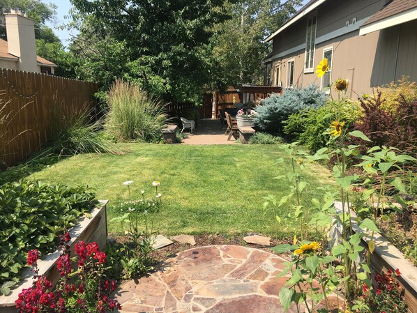Enjoy a serene outdoor space with a patio, lawn, and seating area surrounded by lush plants and a charming fence.