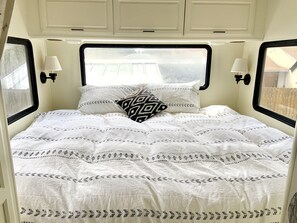 Cozy retreat with a neatly arranged bed and patterned bedspread, featuring a window with a black frame and a wall-mounted lamp on either side.