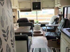 Relax in the motorhome's cozy seating area, featuring a sofa and chair, perfect for unwinding with a view of the outside.