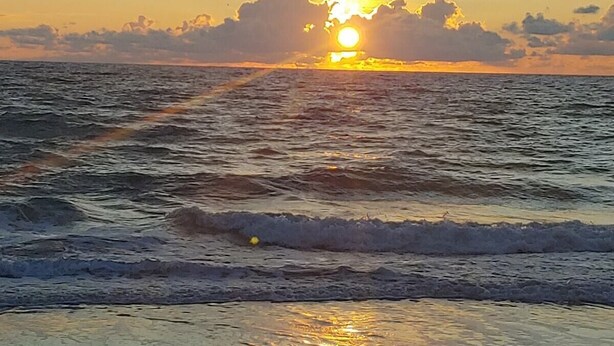 Ein Sonnenuntergang über dem Meer mit Wellen am Ufer.
