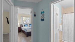 Ein Flur, der zu einem Schlafzimmer führt, mit einem Bett, einem Fenster und einem durch eine geöffnete Tür einsehbaren Badezimmer.