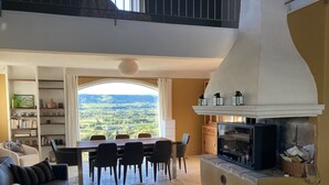 A spacious living room with a high ceiling, a dining area with a view of the countryside, a fireplace, and a television. - Villa provençale 6 pers, Piscine à débordement/Vue exceptionnelle/2 SDB, Ventoux (Villedieu)