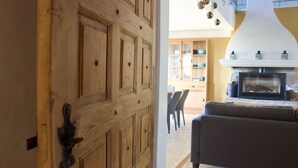 A wooden door with a metal handle, leading to a living room with a fireplace, a sofa, and a dining area with chairs and a table. - Villa provençale 6 pers, Piscine à débordement/Vue exceptionnelle/2 SDB, Ventoux (Villedieu)
