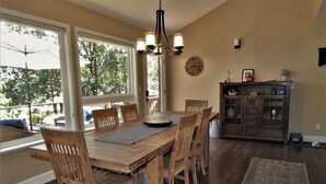 A dining area with a wooden table and chairs, a chandelier, and a view of trees through large windows. - Tree View - Murphys Vacation Rentals (Murphys)