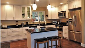A modern kitchen with white cabinets, a stainless steel refrigerator, a microwave, and a large island with stools. - Tree View - Murphys Vacation Rentals (Murphys)