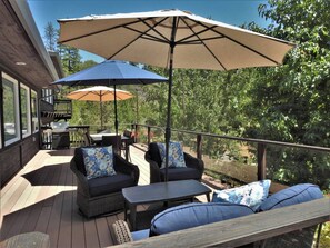 Eine Terrasse mit Gartenmöbeln, darunter Sofas und ein Tisch, sowie zwei Sonnenschirme, die Schatten spenden.