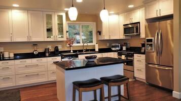 A modern kitchen with white cabinets, a stainless steel refrigerator, a microwave, and a large island with stools.