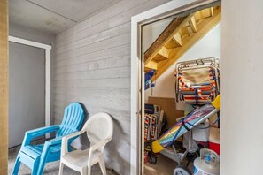 A small room with a wooden ceiling, a white door, and a window. There are two chairs, one blue and one white, and a bunk bed with striped bedding.