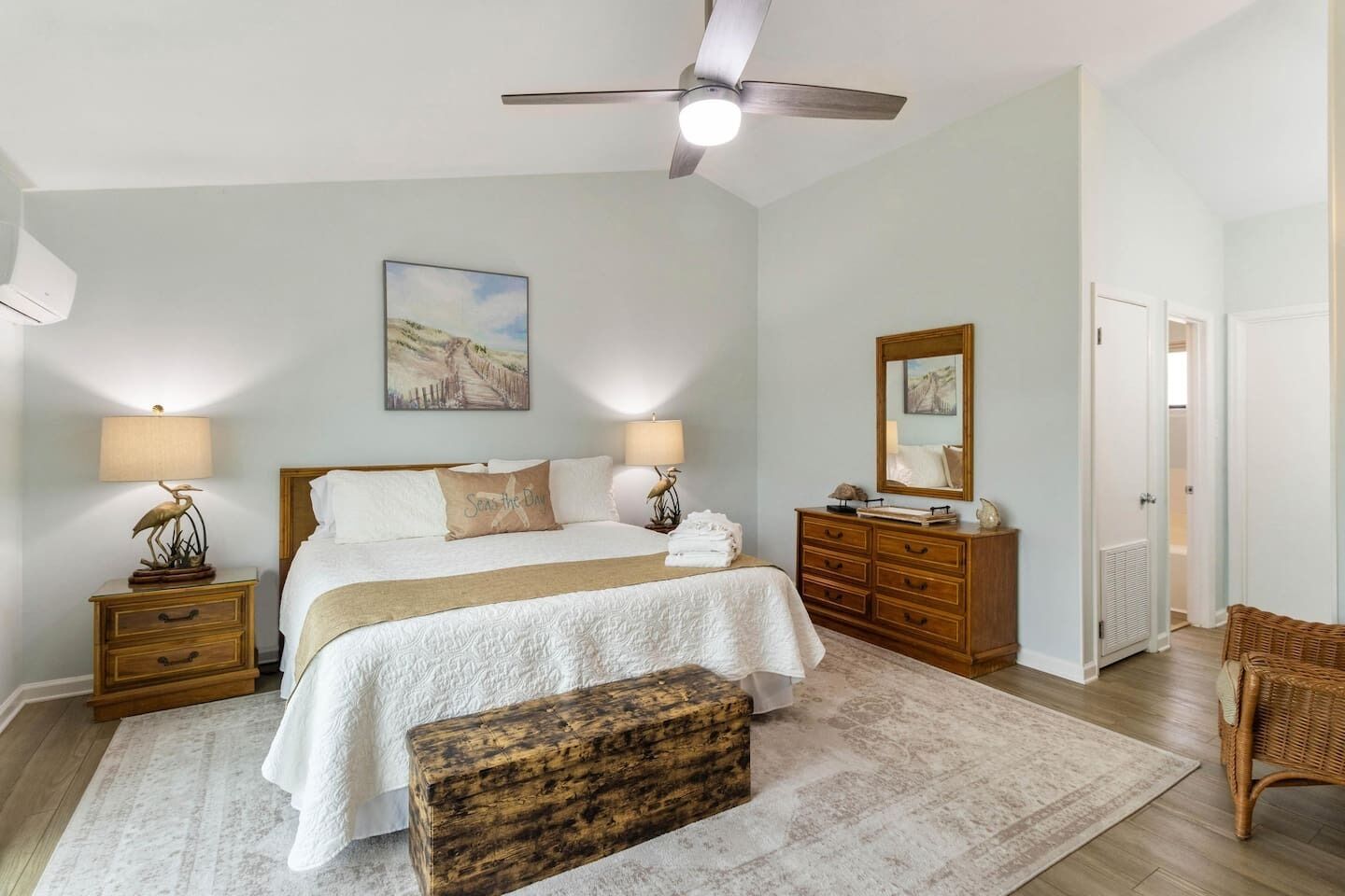 A bedroom with a bed, bedside tables, a dresser, a mirror, a ceiling fan, and a door.
