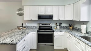 A kitchen with white cabinets, a stainless steel oven, a microwave, and a marble countertop.