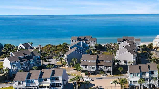 A coastal residential area with multi-story buildings, a clear view of the ocean, and a paved road.