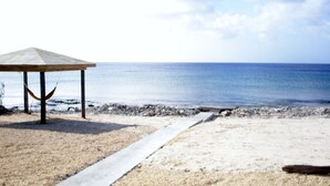 A beach with a wooden structure, a hammock, and a concrete path leading to the water.