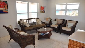 A living room with wicker furniture, a coffee table, and a view of the sea through large windows.