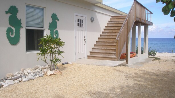 A coastal house with a wooden staircase leading to a covered porch overlooking the sea.