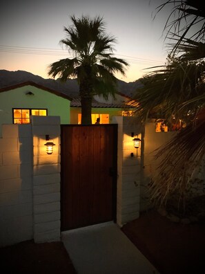 Een huis met een houten poort, een palmboom en twee lantaarns aan de muur.